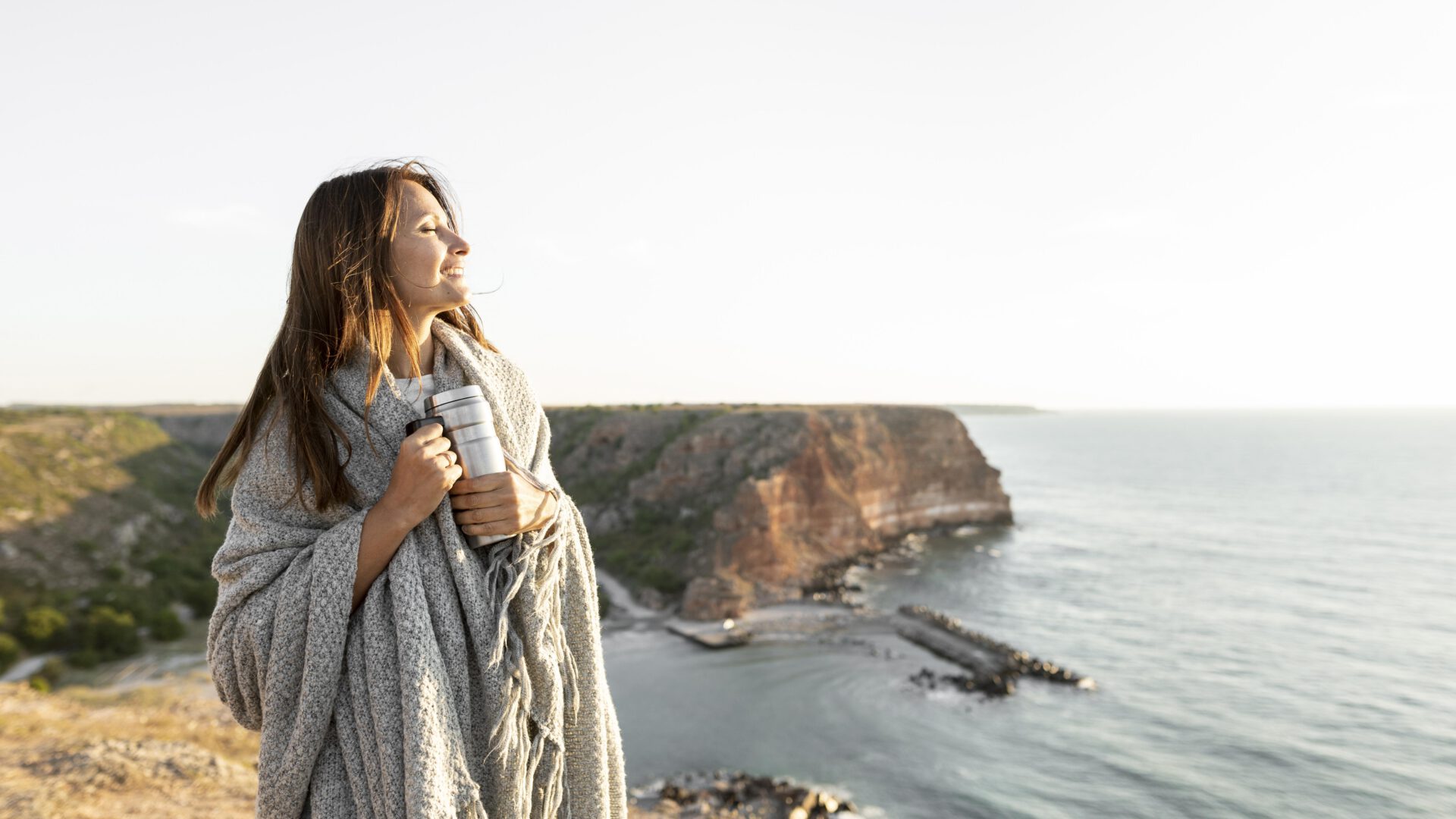 woman-holding-thermos-while-walking-coast-with-copy-space